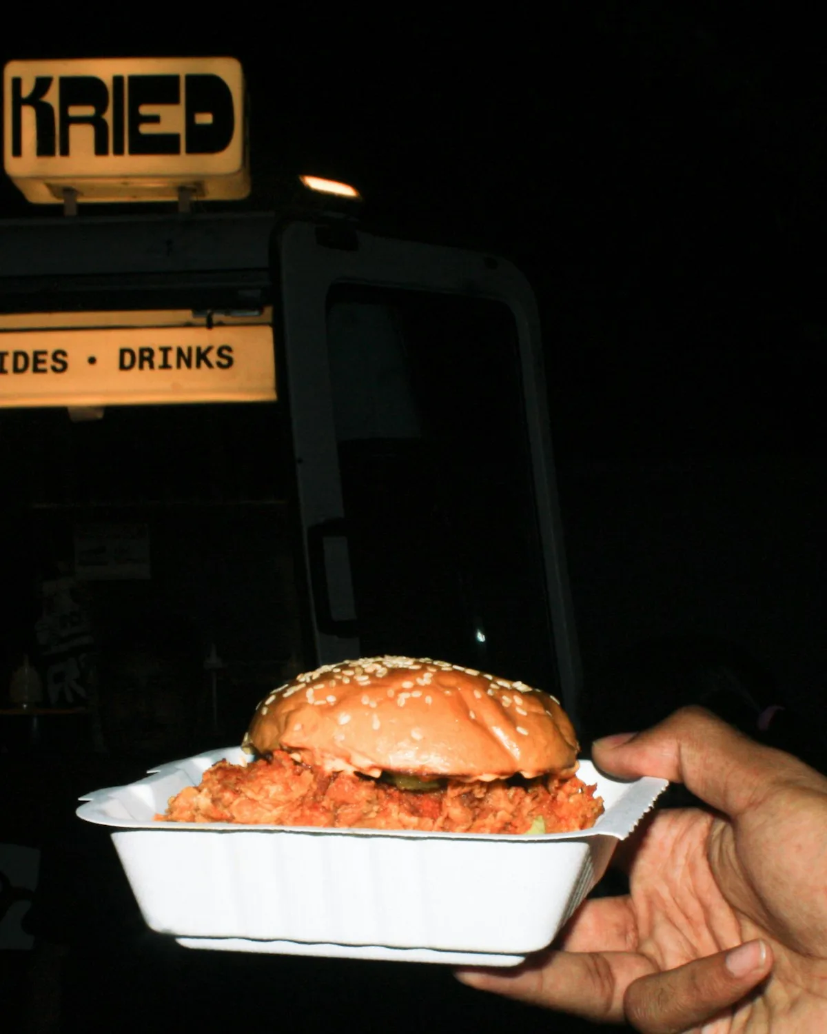 A fried chicken burger handed over in a takeaway box outside a food truck