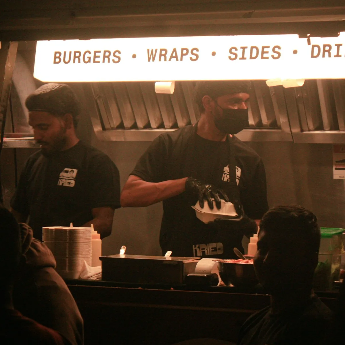 Two cooks working the hatch of a lit food stall at night